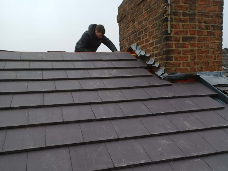 Roofer fitting stepped lead flashing to a brick chimney on a new slate roof