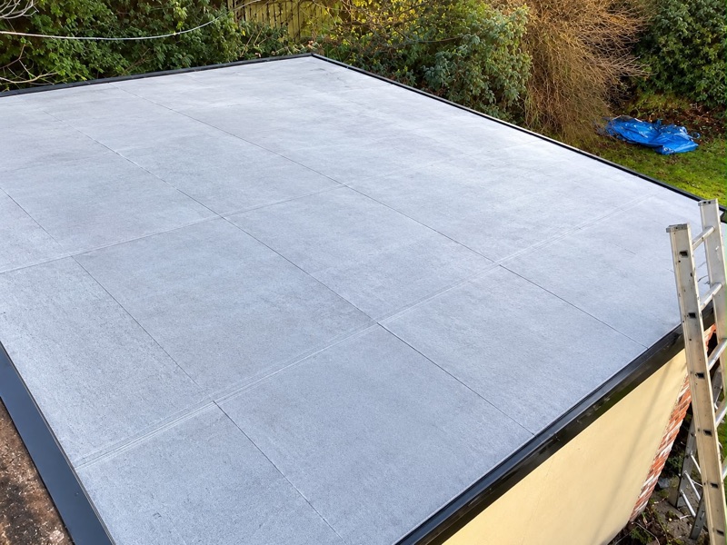 New grey fibreglass flat roof on a single-storey extension, with black edge trims and a ladder to the side