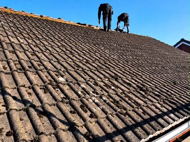 Two roofers stripping old moss-covered concrete tiles from a roof