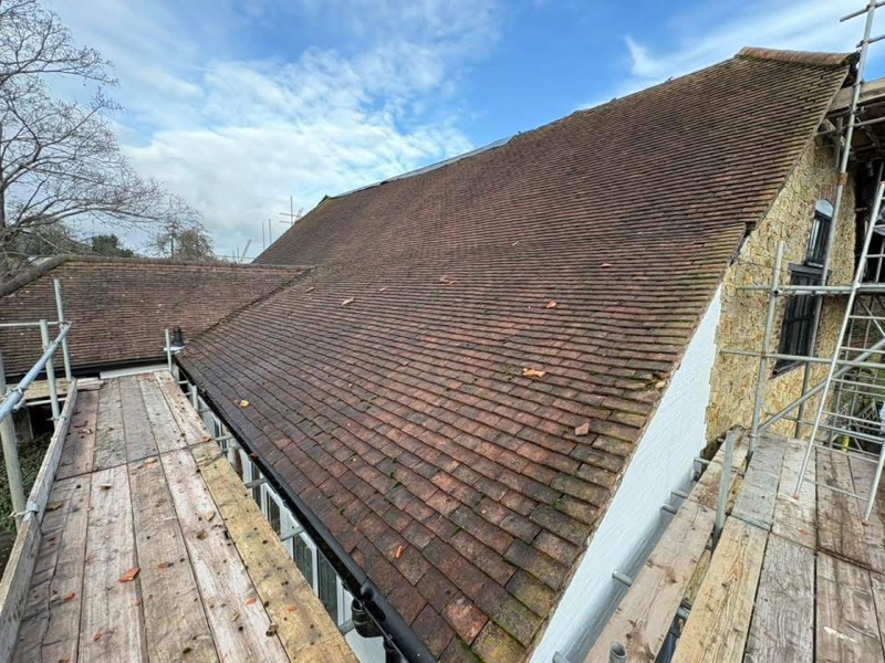 Old weathered plain-tile roof with scaffolding around the house